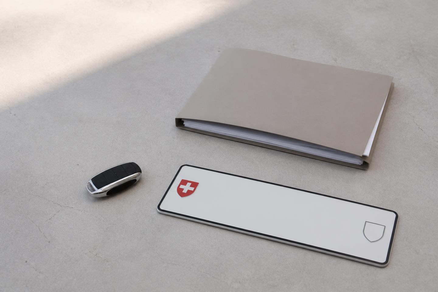 Car key, a folder of vehicle documents and a Swiss licence plate on a light surface
